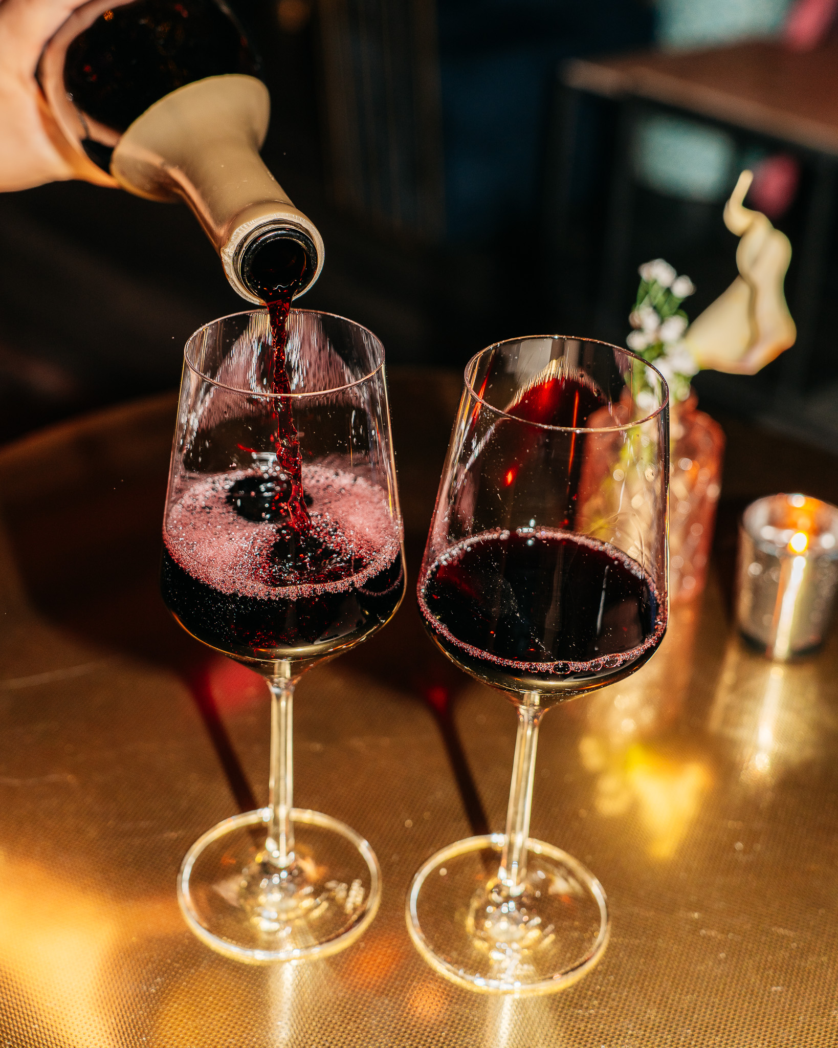 Red wine pouring from bottle into glass, second glass nearby.
