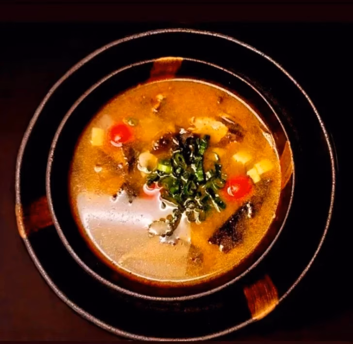 Overhead view of soup in a dark bowl with green onions and tomatoes.