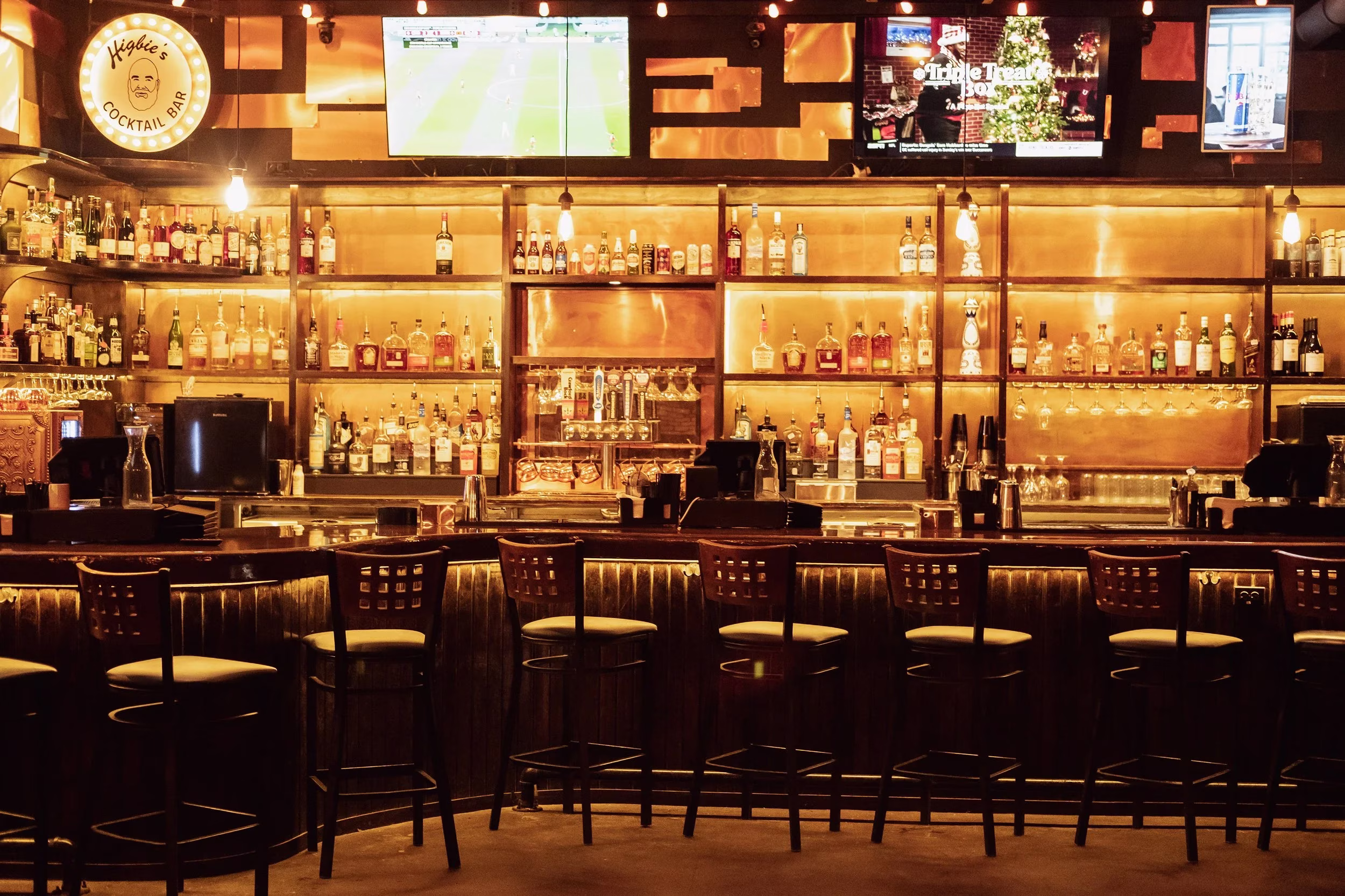 Higbie's Cocktail Bar interior with bottles, bar stools, and screens.