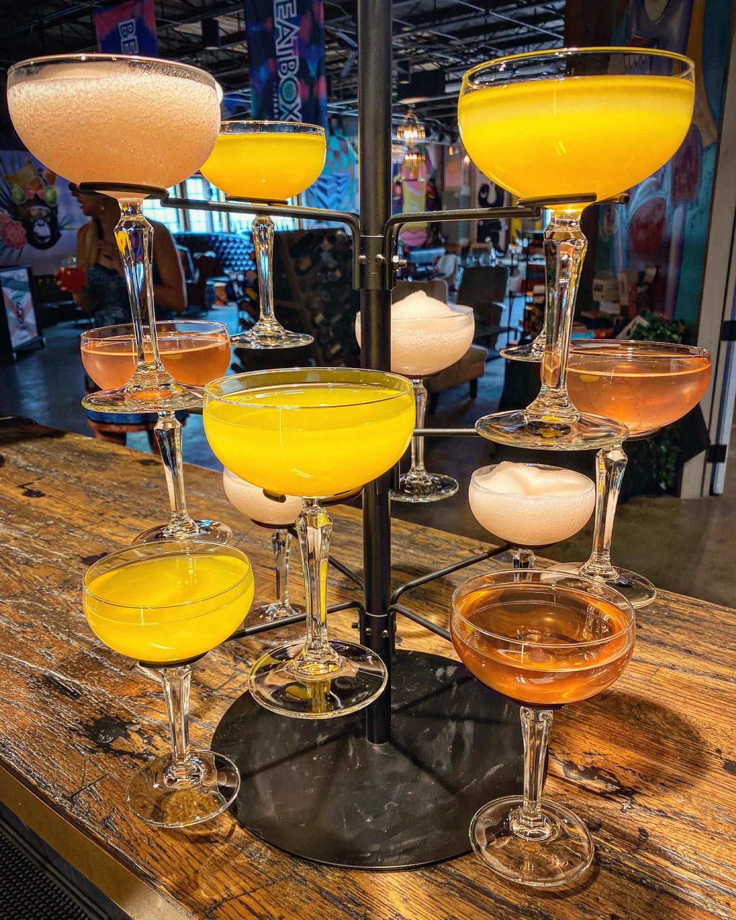 Multiple coupe glasses with colorful cocktails on a tiered stand.