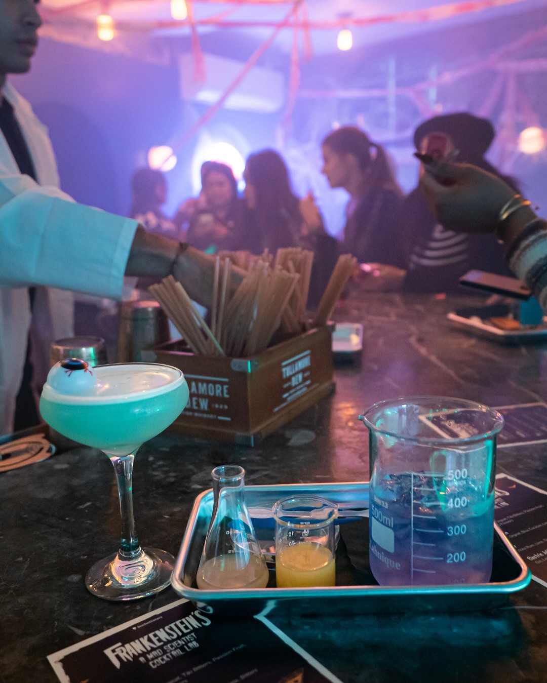 Bartender in lab coat serves themed drinks in scientific glassware at a bar.