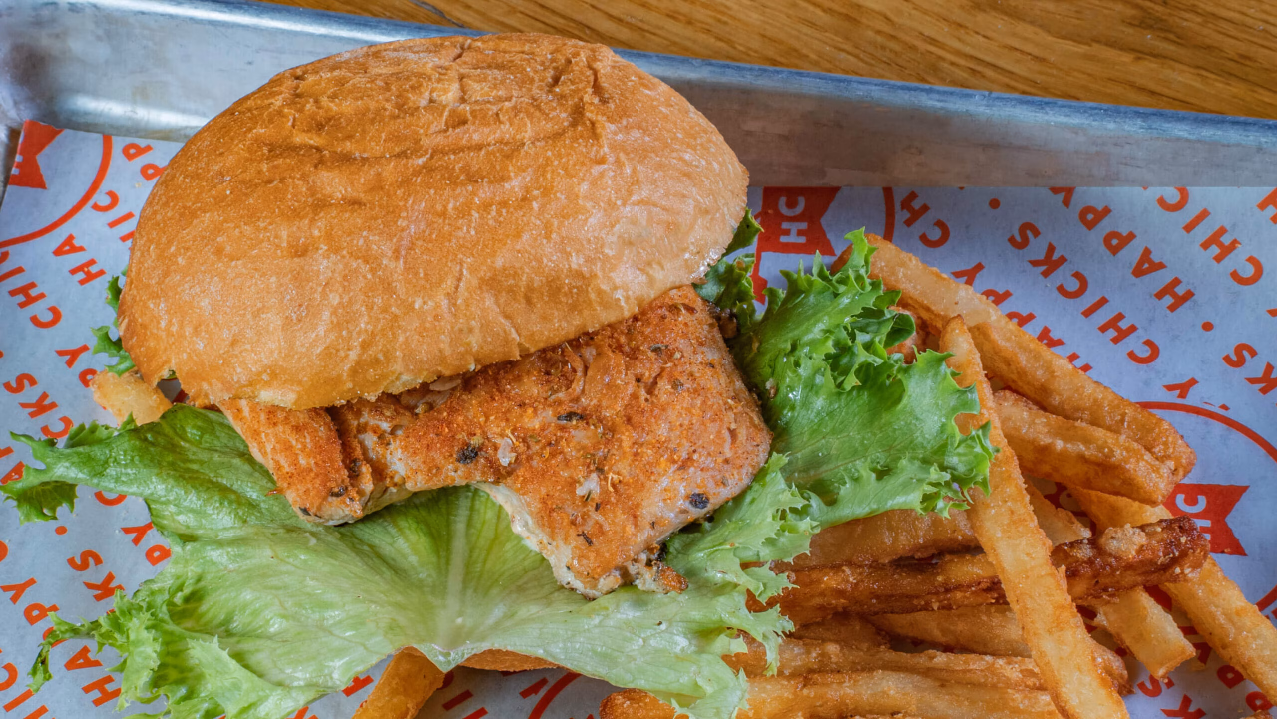 Fried chicken sandwich with lettuce and french fries on a tray.
