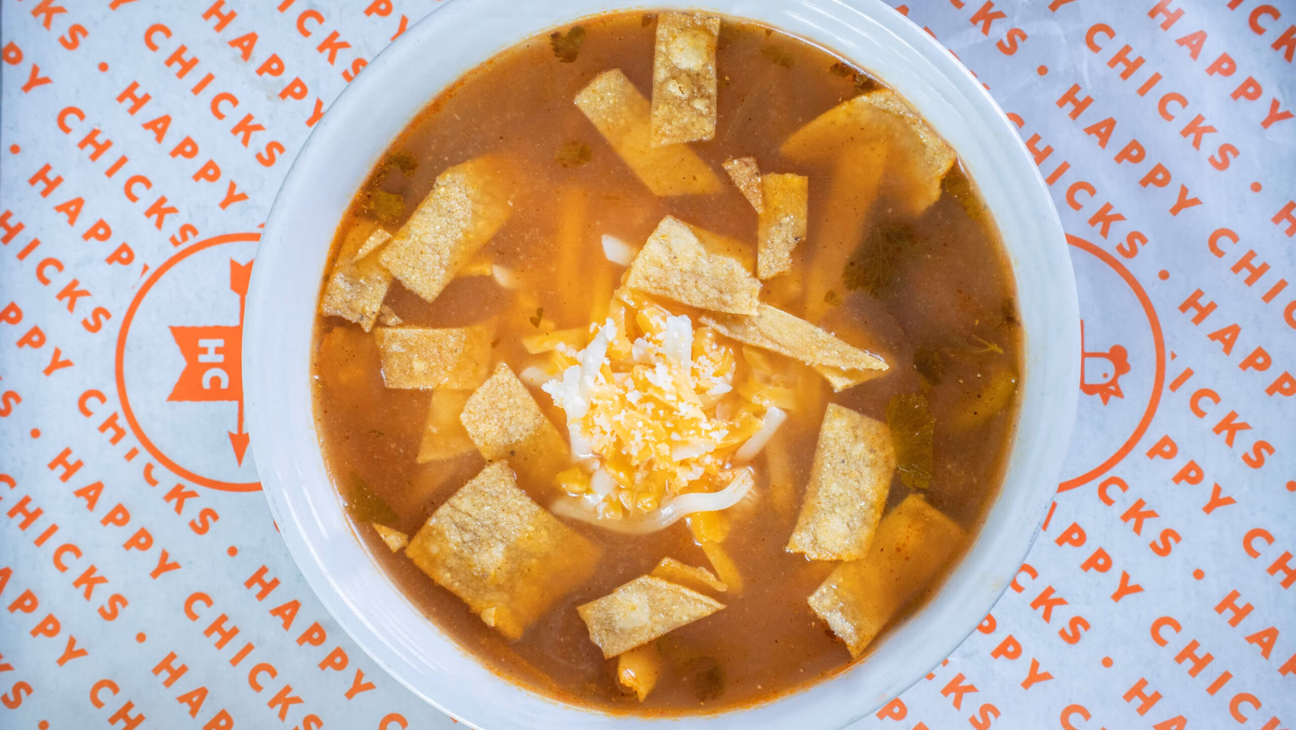 Chicken tortilla soup in a white bowl on Happy Chicks paper.