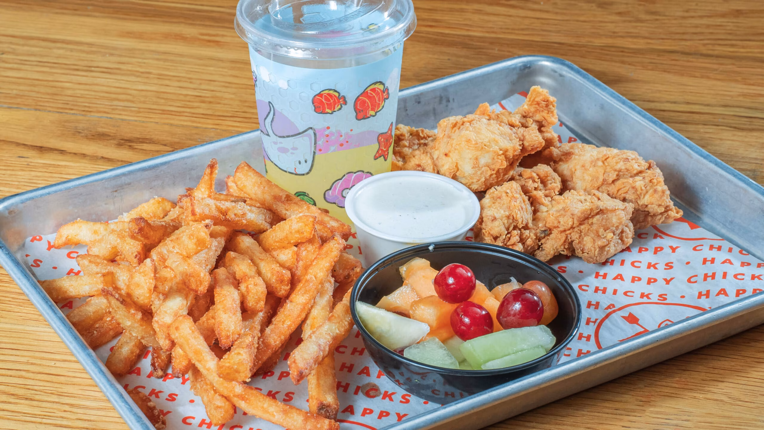 Fried chicken, french fries, fruit, sauce, and drink on tray.