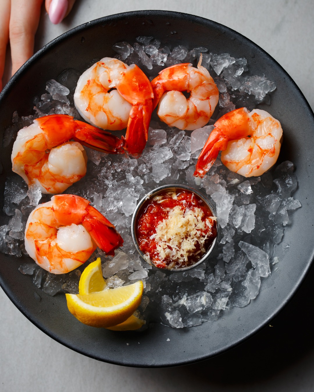 Shrimp cocktail with sauce and lemon served on crushed ice.