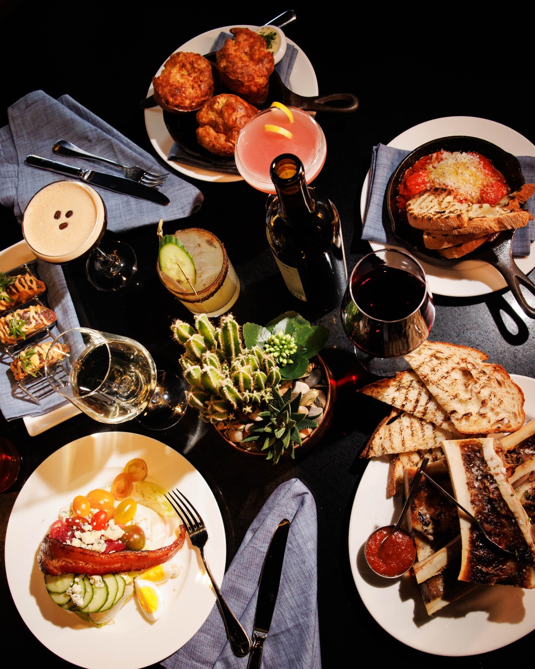 Table filled with various restaurant dishes, cocktails, and wine.