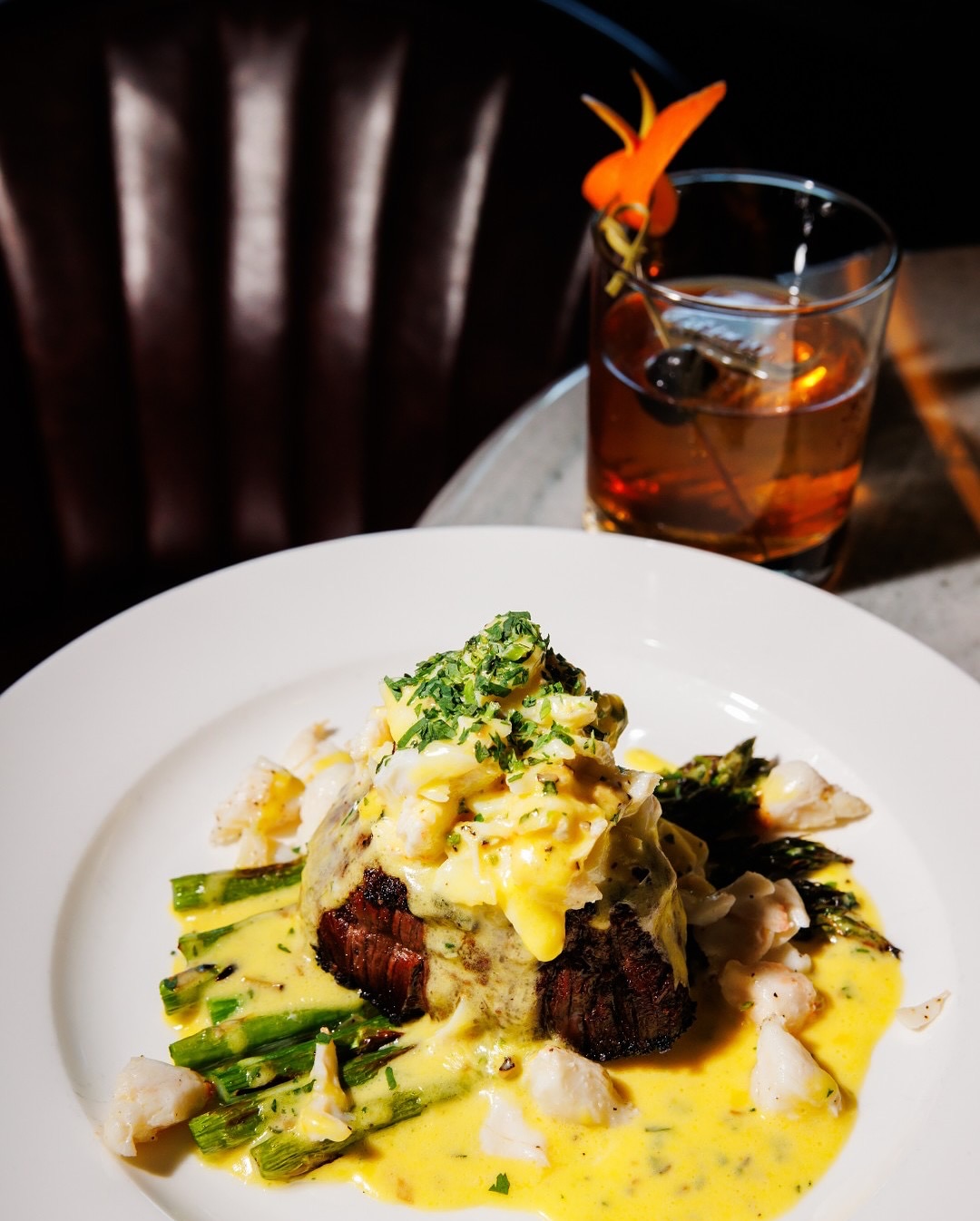 Steak topped with crab, asparagus, yellow sauce, and a cocktail.