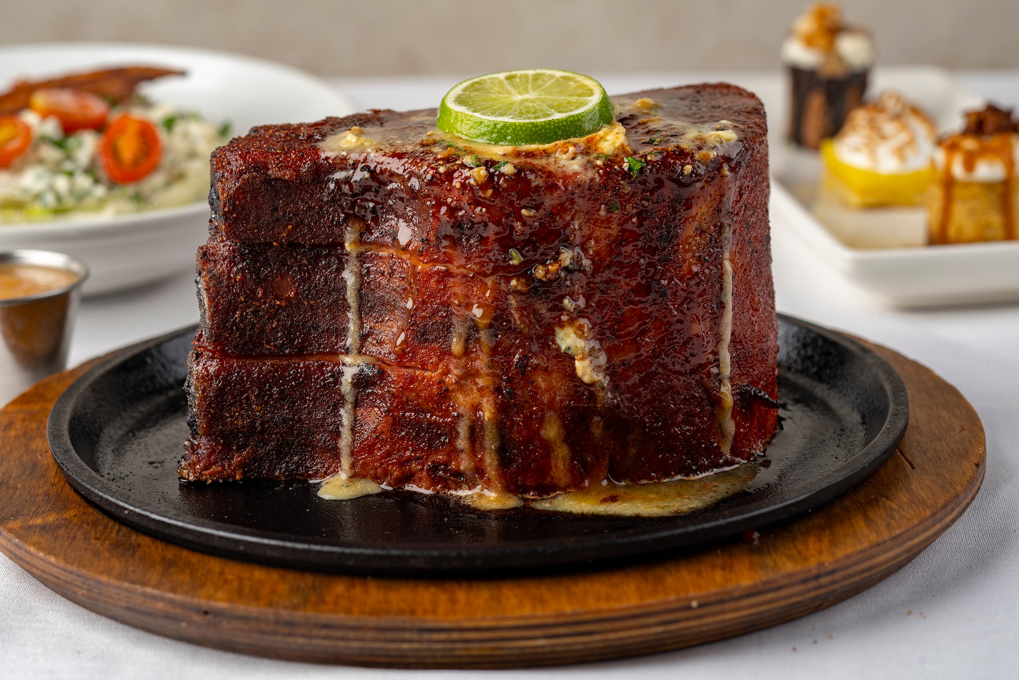 Thick glazed meat block with lime slice on a hot skillet.
