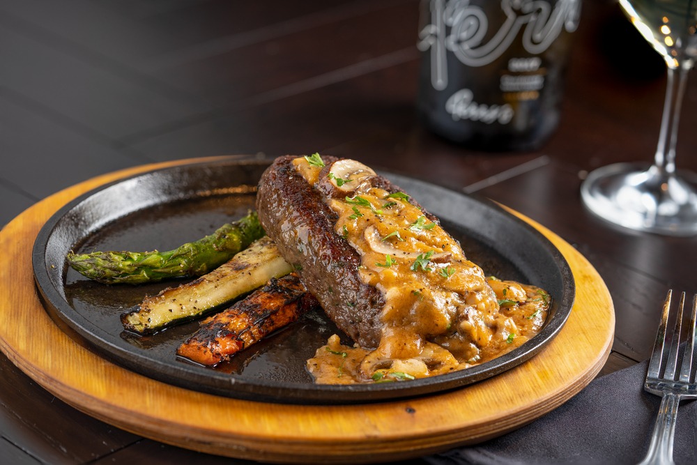Steak with mushroom sauce, asparagus, and roasted vegetables on a cast iron plate.