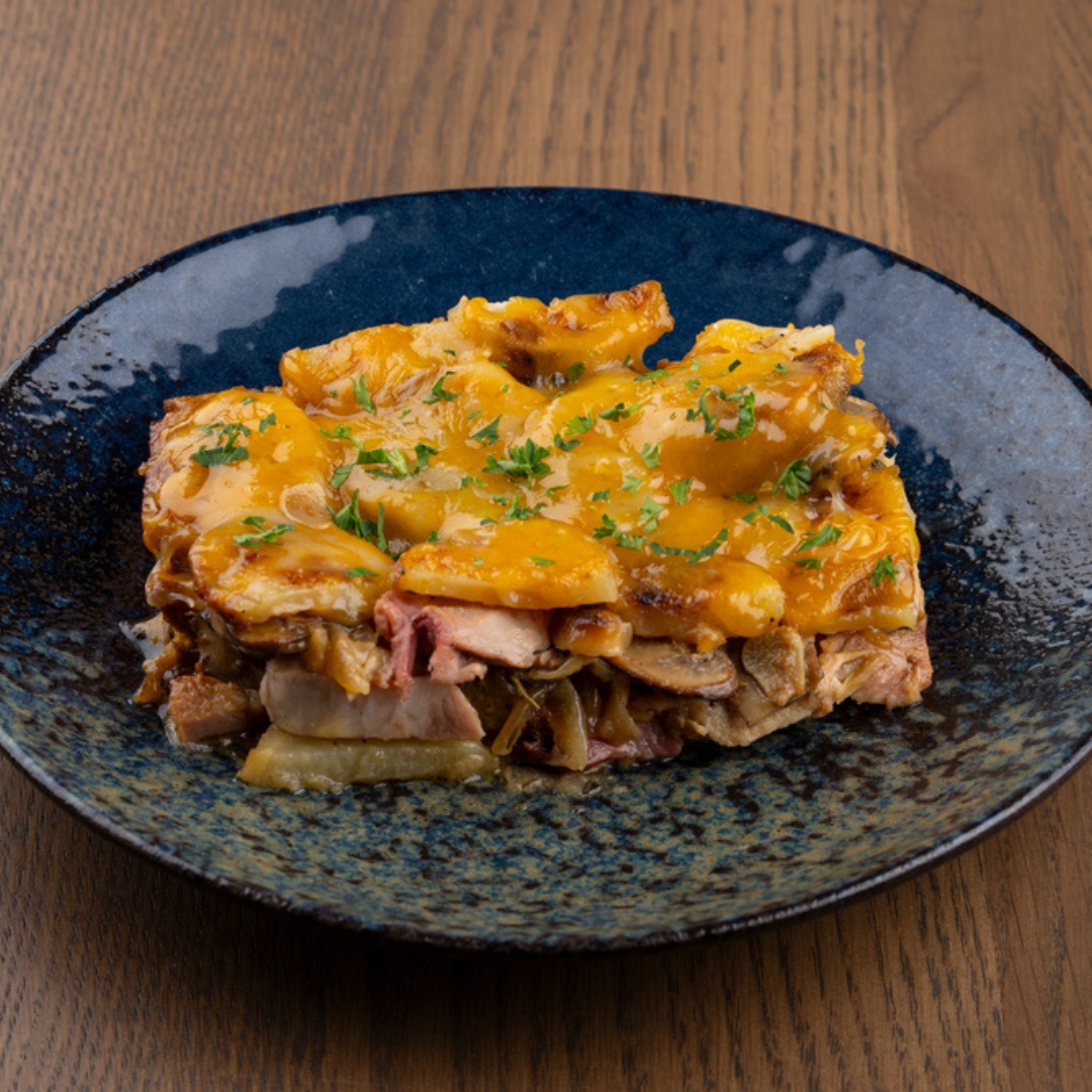 Rectangular gratin with sliced potatoes, melted cheese, meat, mushrooms, parsley.