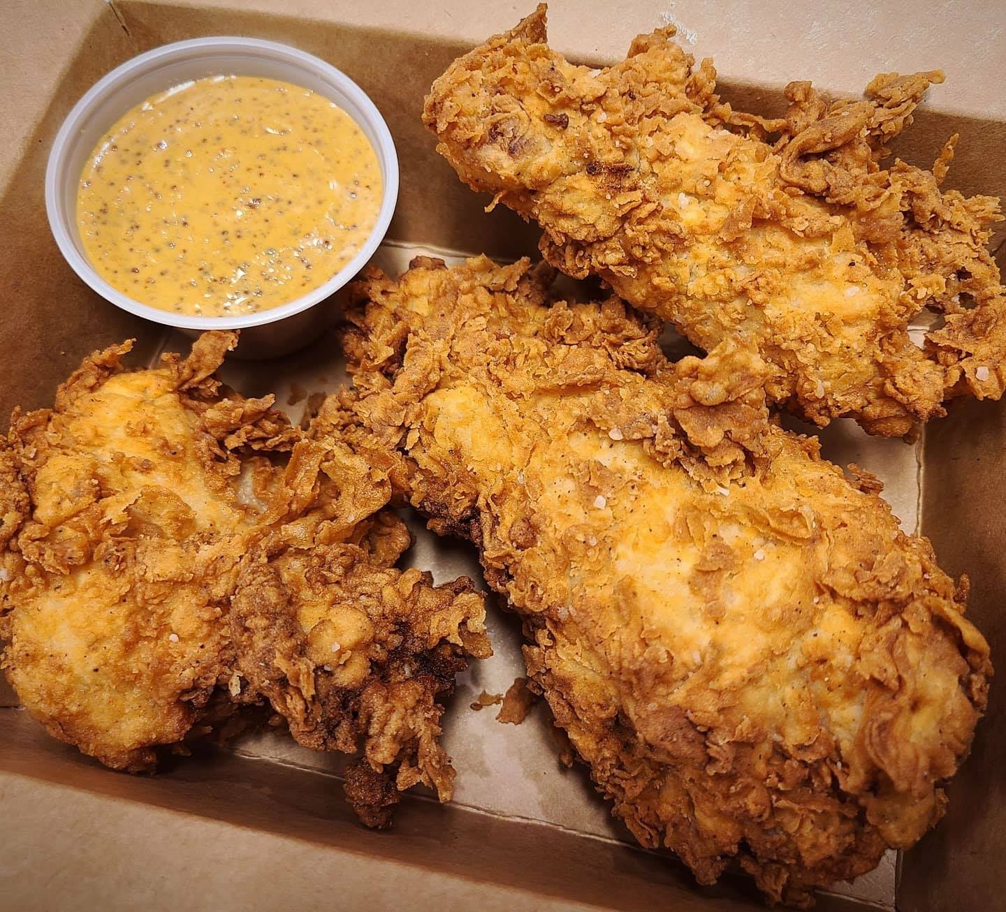 Fried chicken tenders with dipping sauce in a cardboard box.