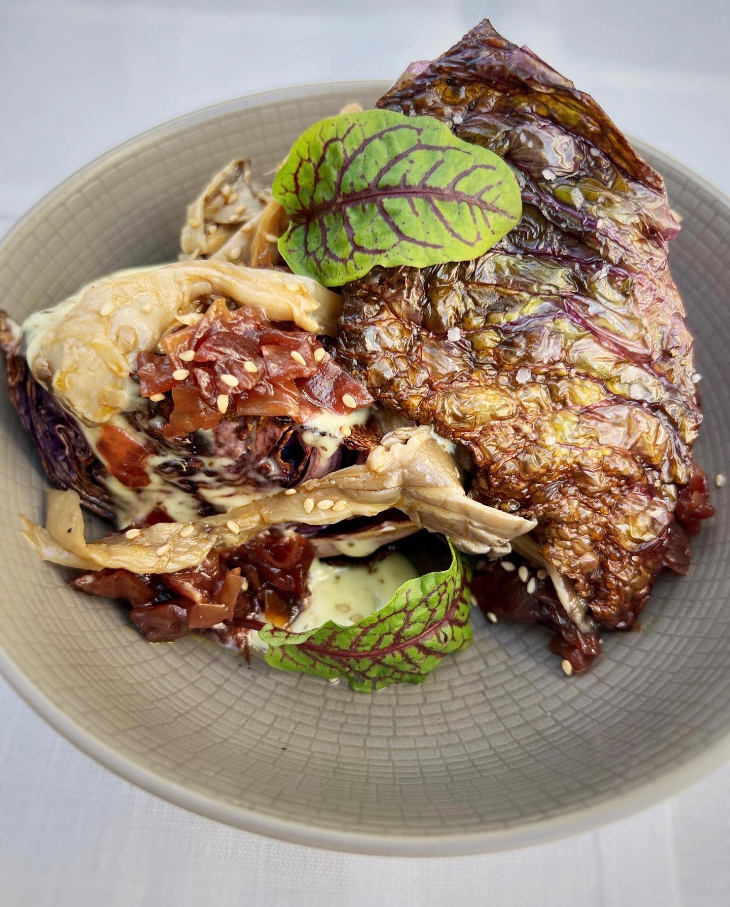 Cooked dark cabbage dish with creamy sauce, sesame seeds, and green garnish.