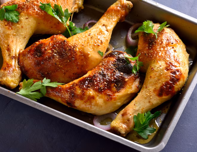 Roasted chicken drumsticks and thighs with herbs and onion in a pan.