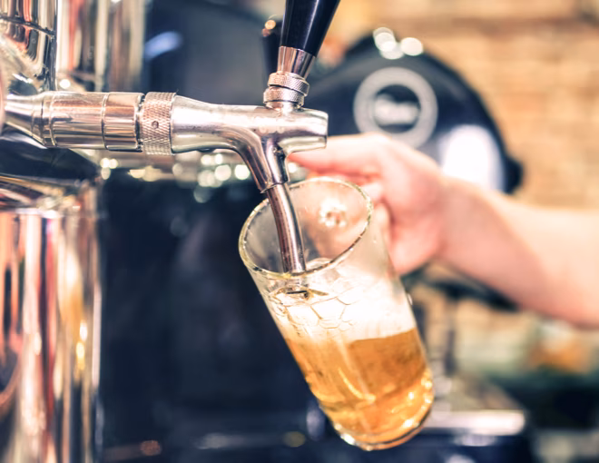 Hand holding a glass under a tap pouring golden beer.