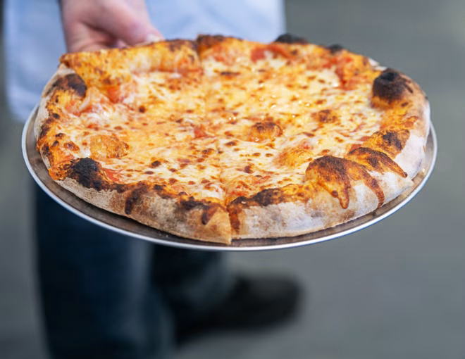 Person holding a cheese pizza with a bubbly, charred crust.