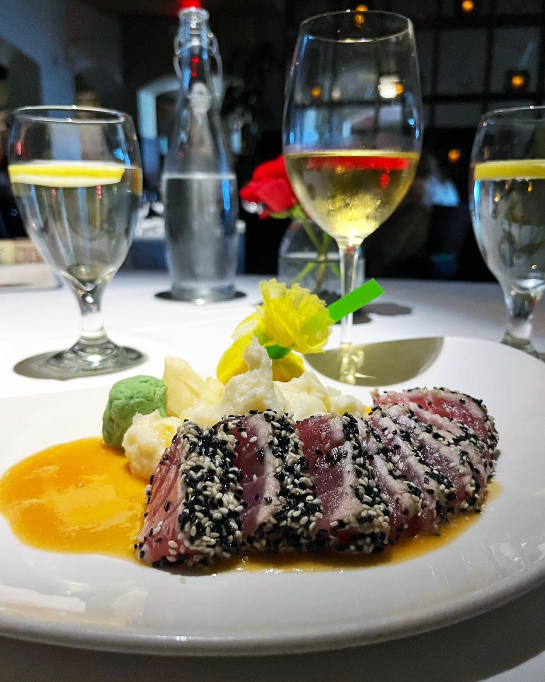 Plate of seared sesame-crusted tuna with sauce and white wine.