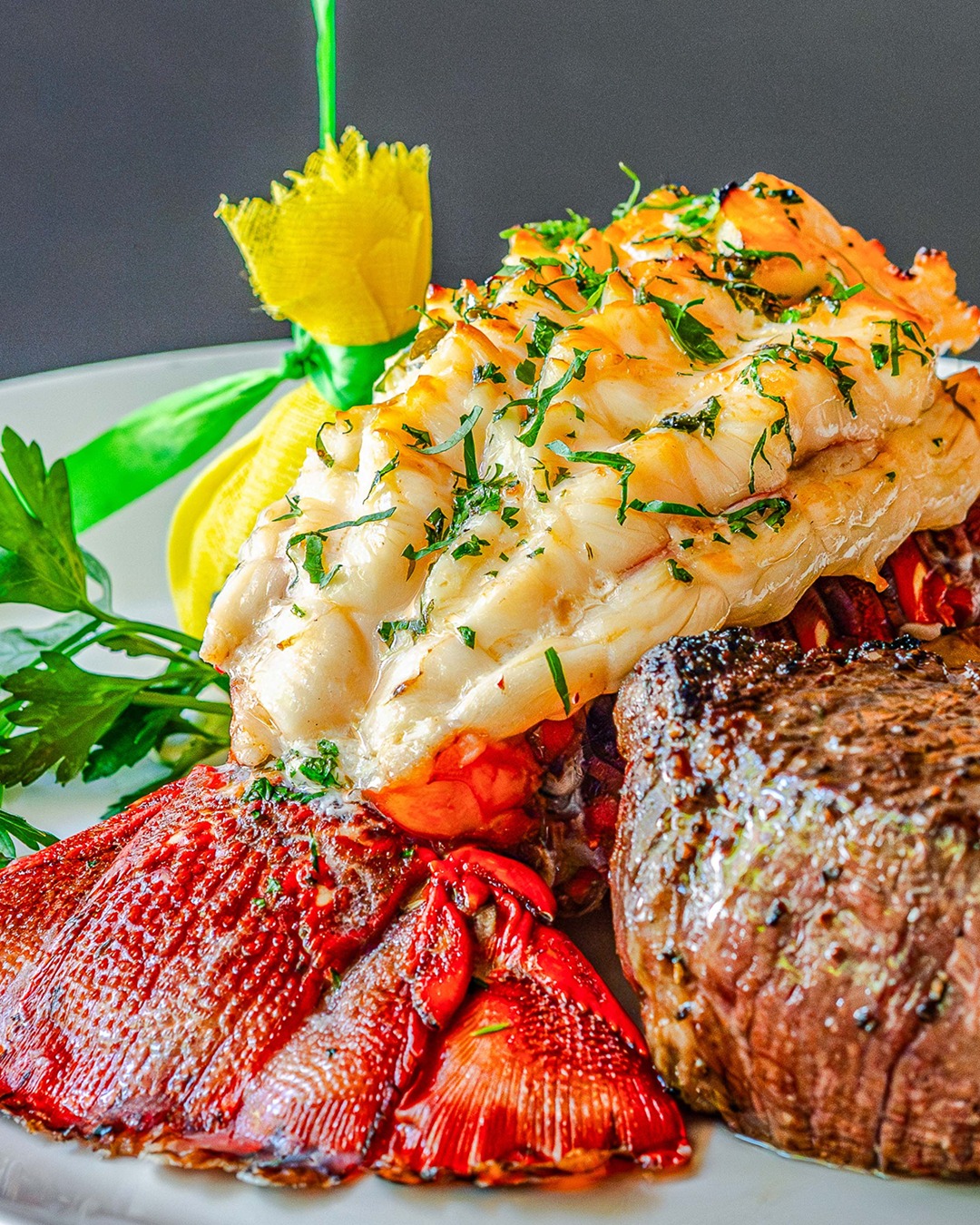 Steak and broiled lobster tail with fresh parsley and a lemon.
