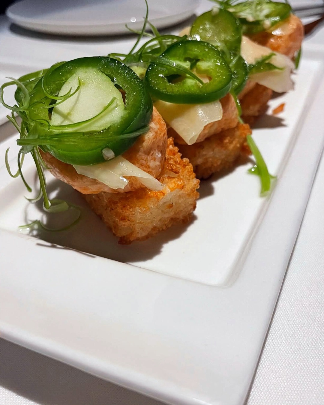 Crispy rice with salmon, jalapeño, and green onion on a plate.