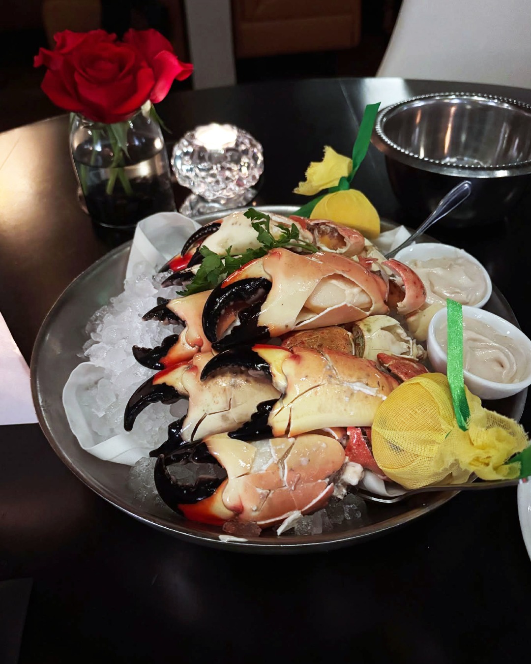Cooked crab claws served on ice with sauces, lemon, and a rose.