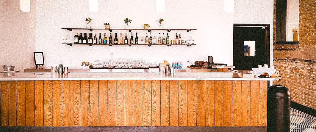Modern bar with wood paneling, metal counter, bottles, and glasses.