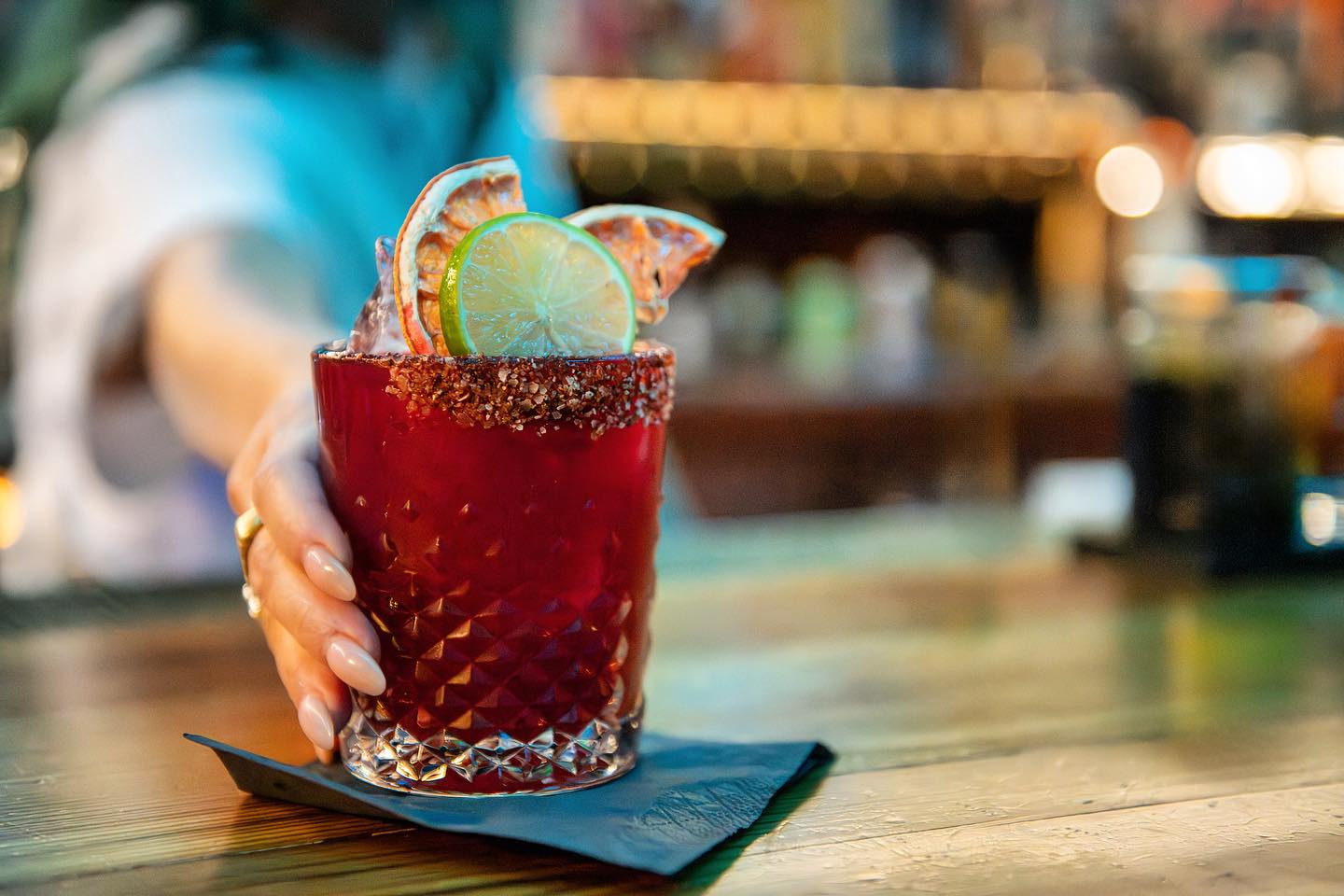 A woman holds a red cocktail garnished with lime and dried orange.