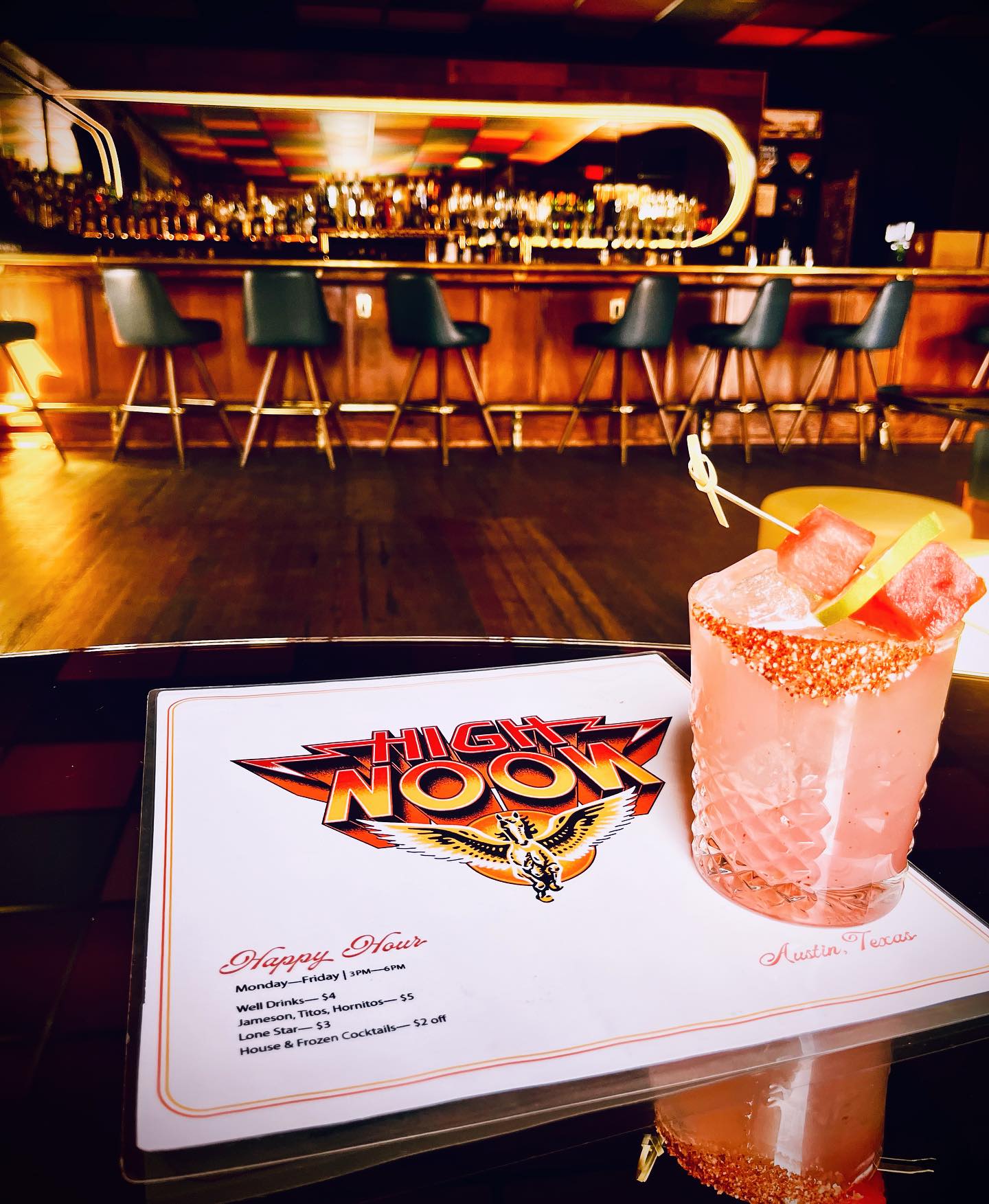 Pink cocktail with fruit garnish, happy hour menu, blurred bar.
