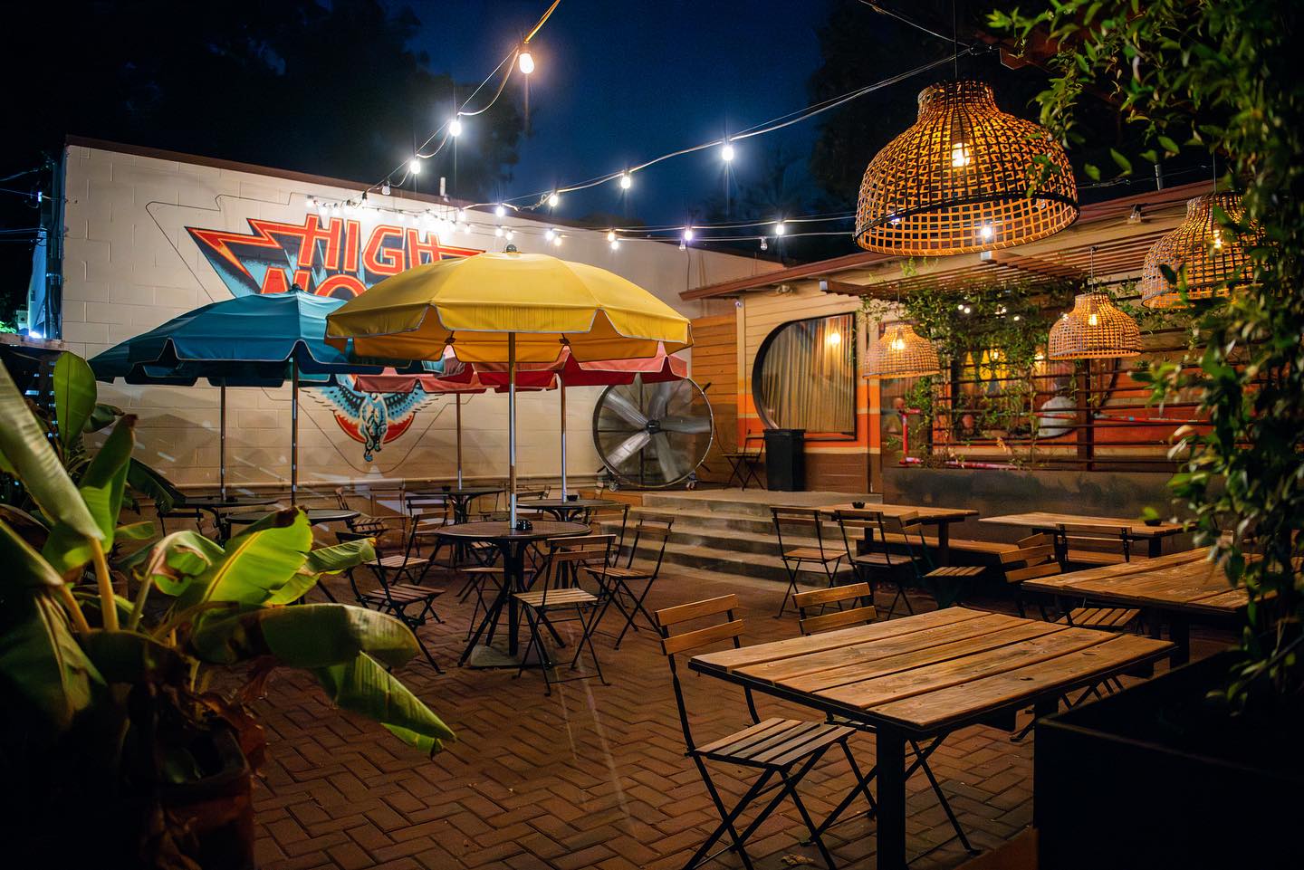 Nighttime outdoor dining patio with tables, umbrellas, and string lights.