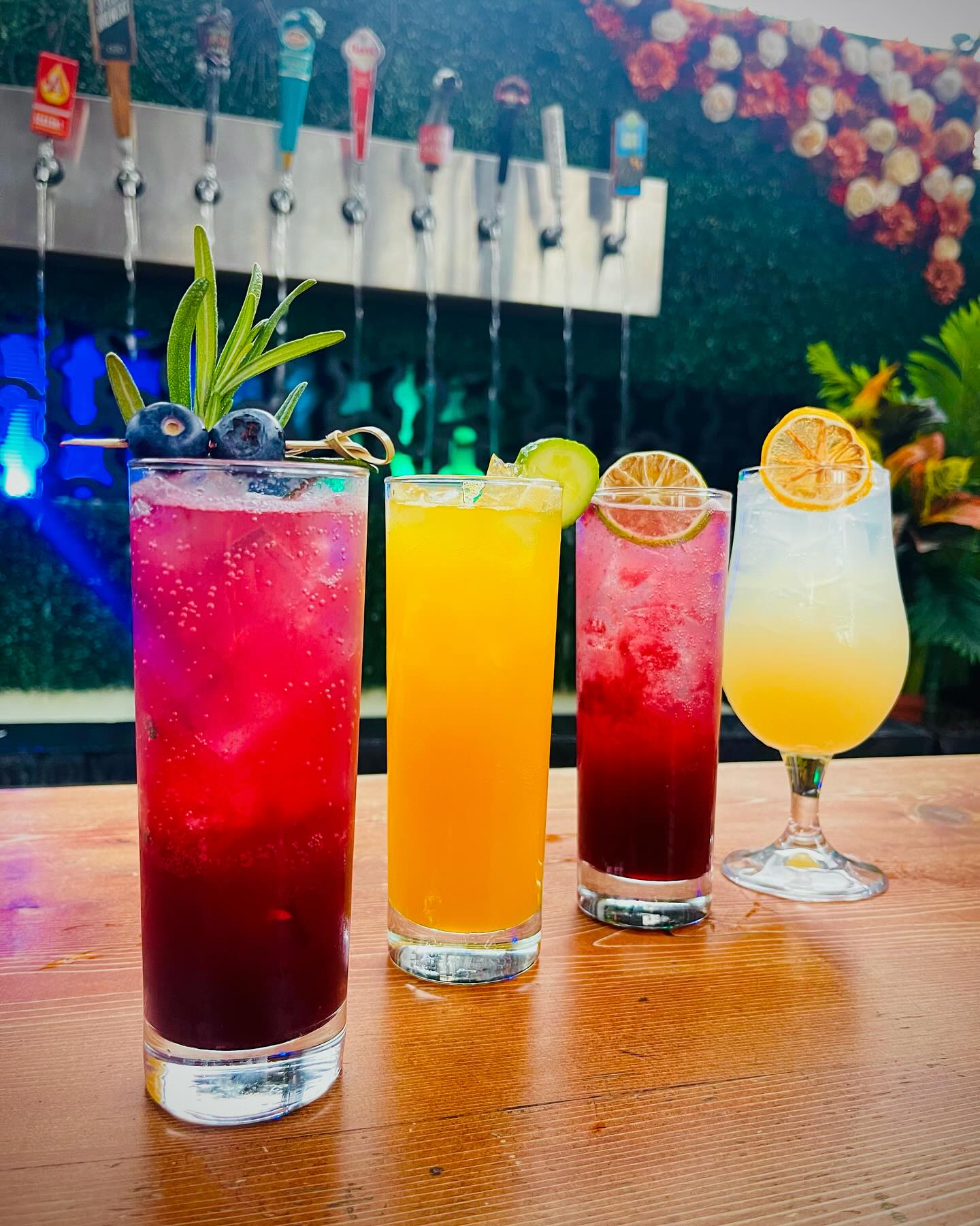 Four colorful drinks with garnishes on a wooden bar counter.