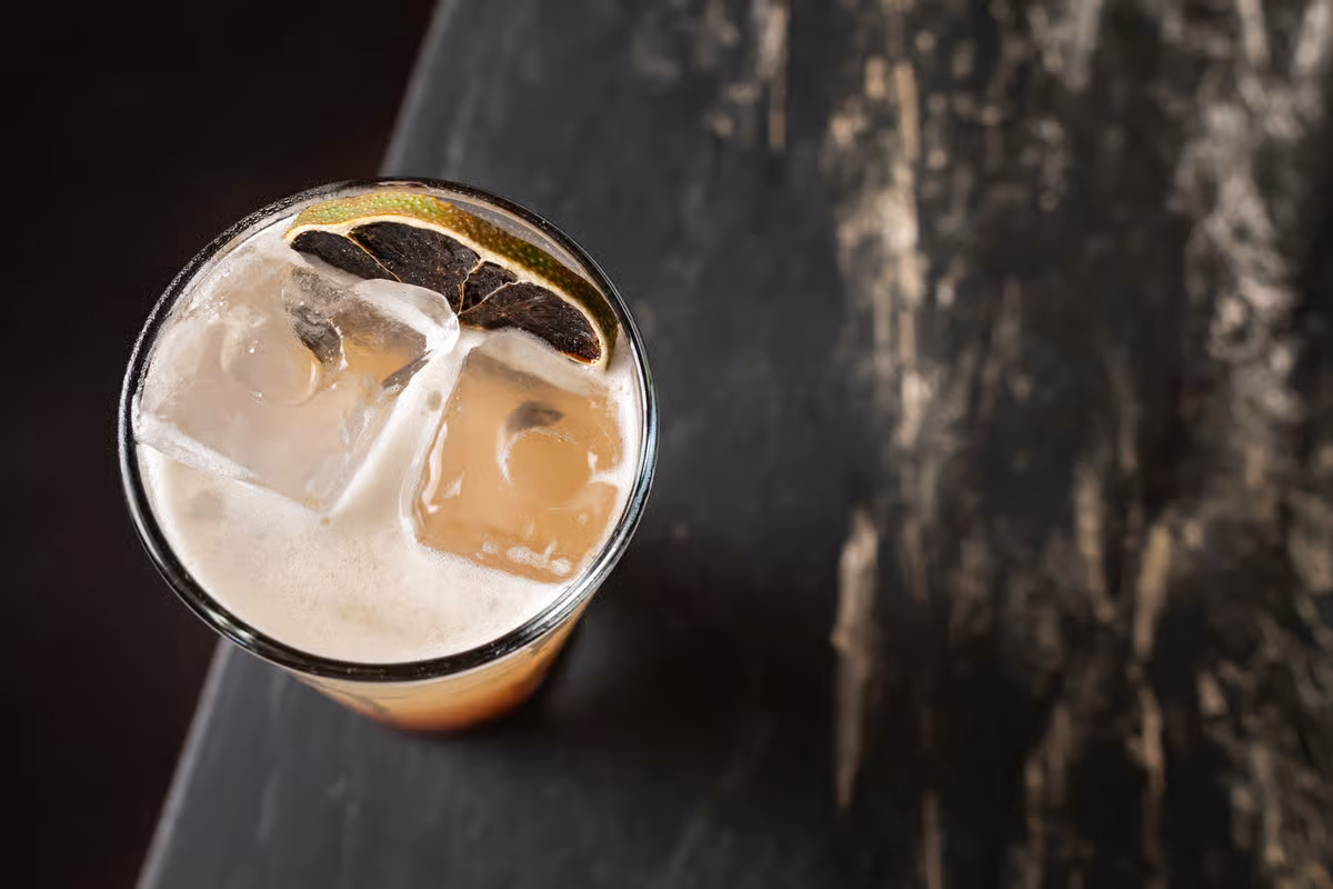 Glass of foamy drink with ice and a dried lime slice.