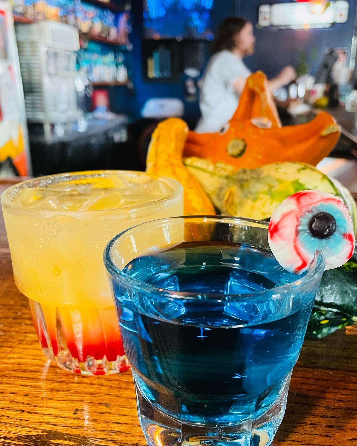 Yellow iced drink and blue shot with gummy eyeball on bar.
