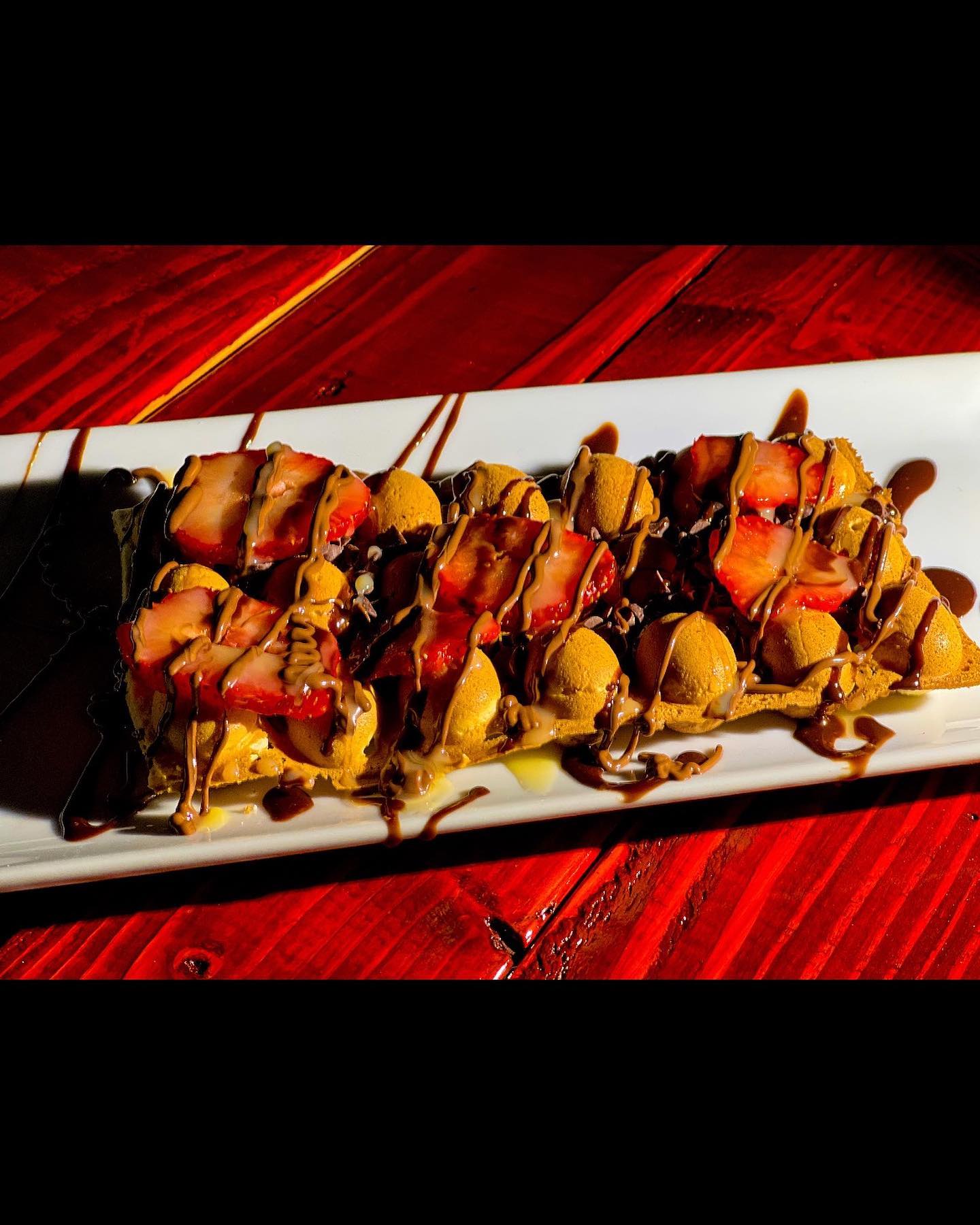 Bubble waffle with strawberries, golden pastry balls, and chocolate drizzle.