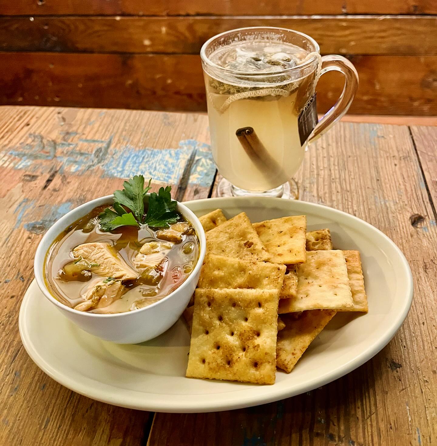 Soup, crackers, and warm drink with cinnamon stick on wooden table.