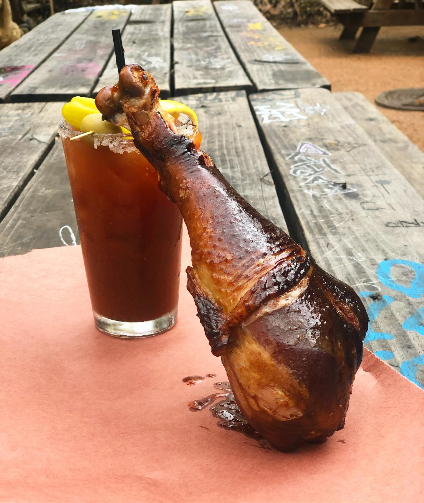 Dark roasted turkey leg next to a Bloody Mary cocktail outdoors.