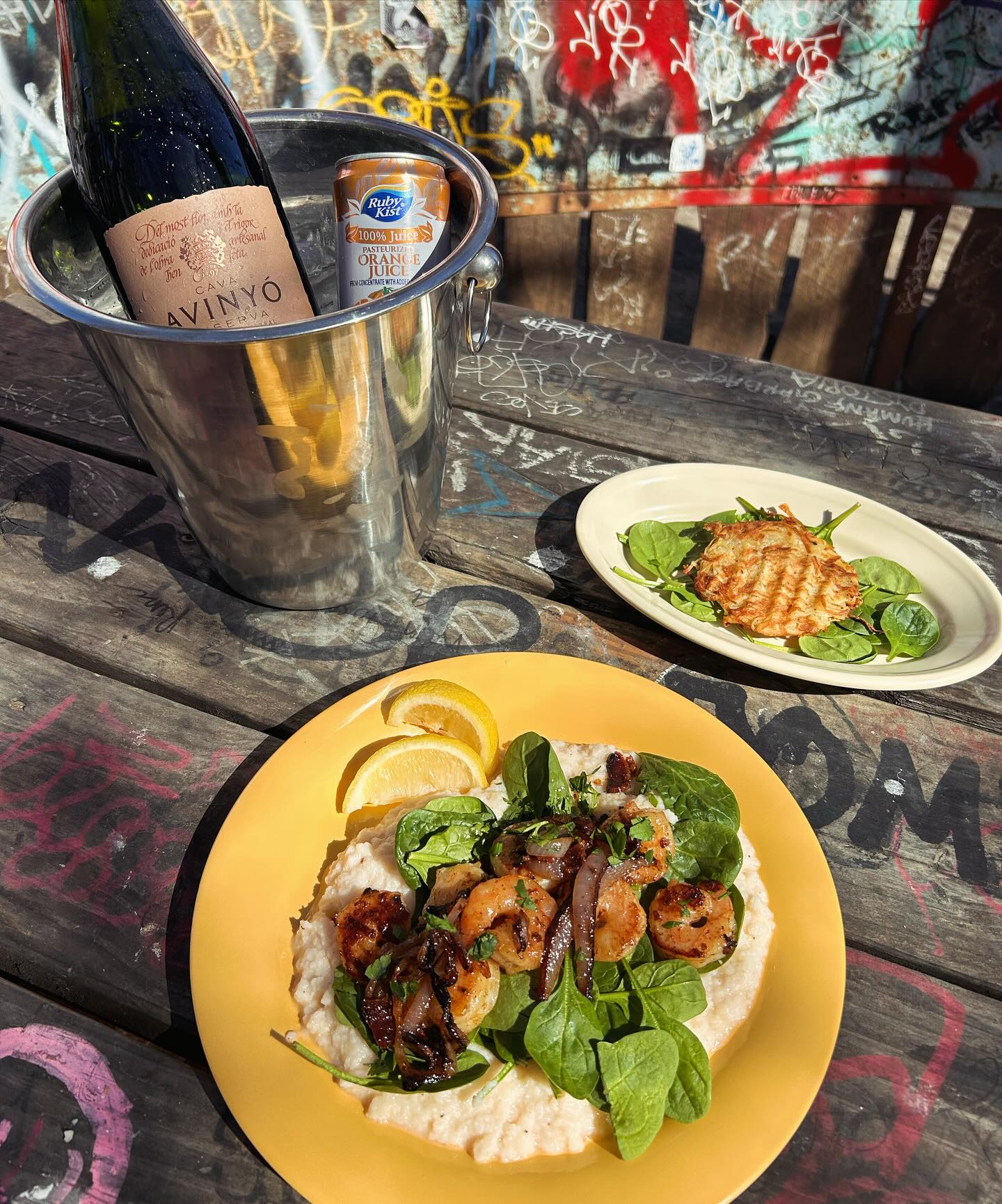 Shrimp and grits, hash brown, cava, and juice on a graffiti table.