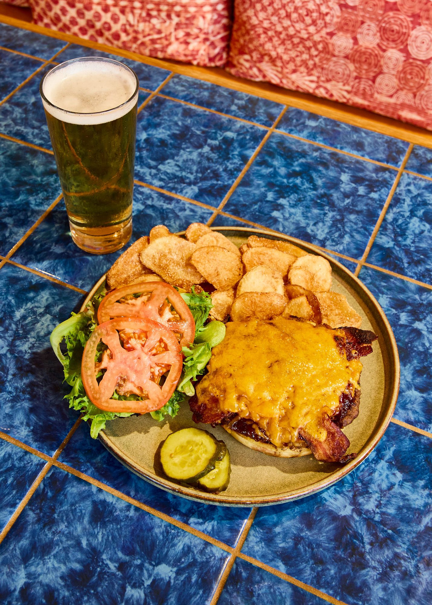 Cheeseburger, potato chips, lettuce, tomatoes, pickles, and a glass of beer.