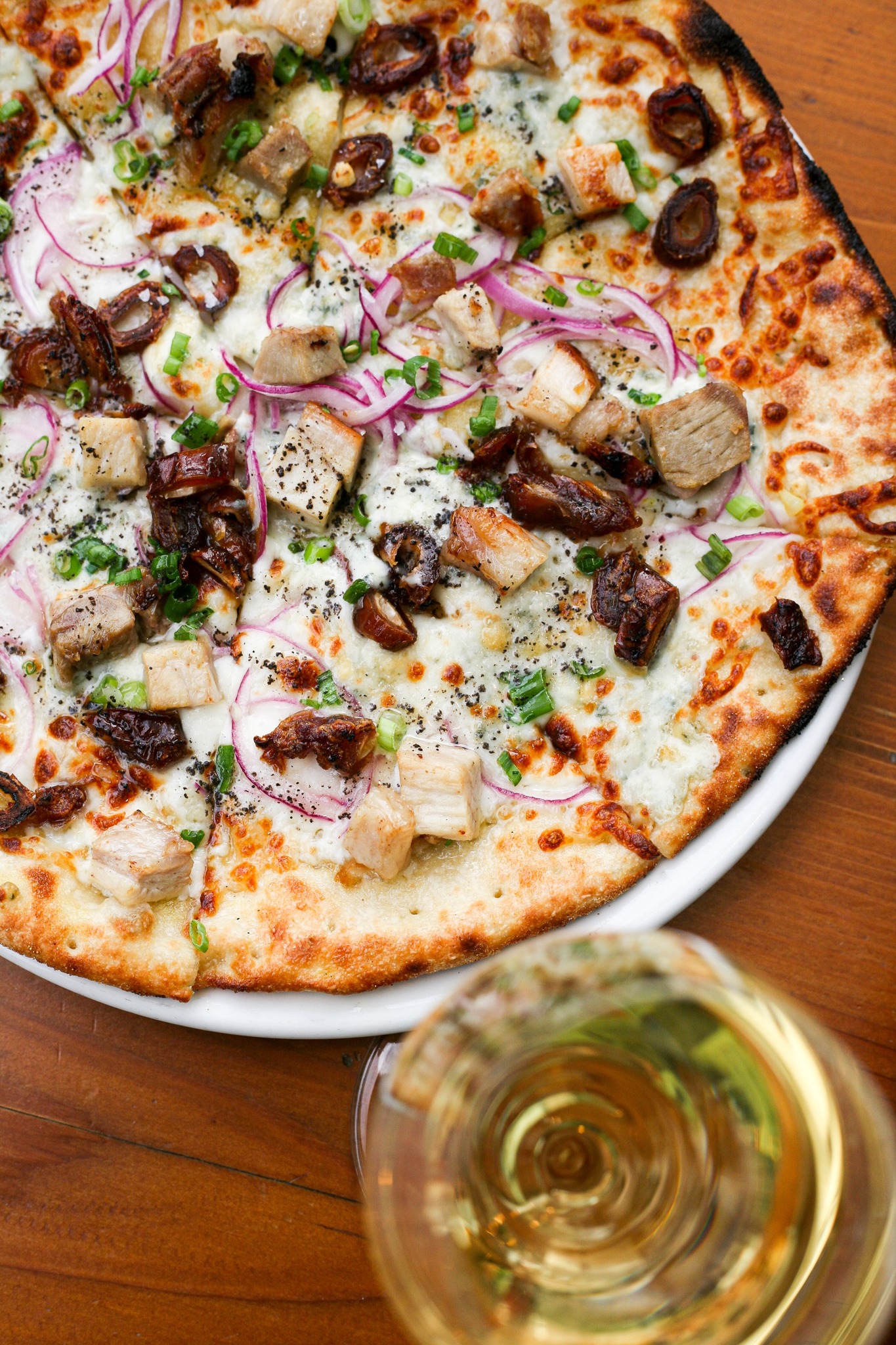Pizza topped with meat, dried fruit, red onion, and white wine.