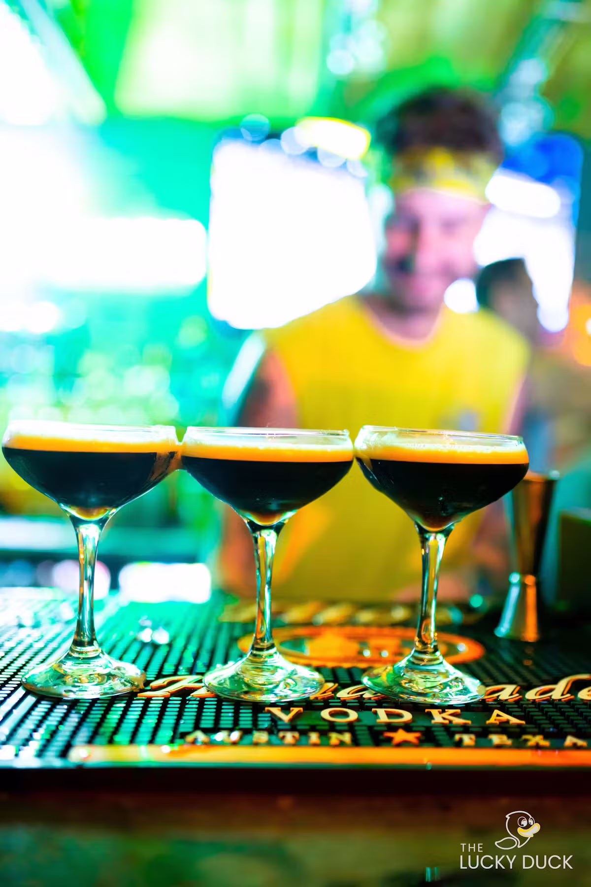 Three dark cocktails in martini glasses on a 'VODKA' bar mat.