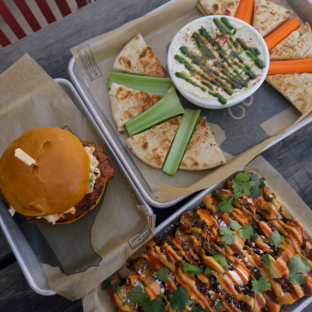 Three trays of food: a sandwich, hummus, and loaded fries.