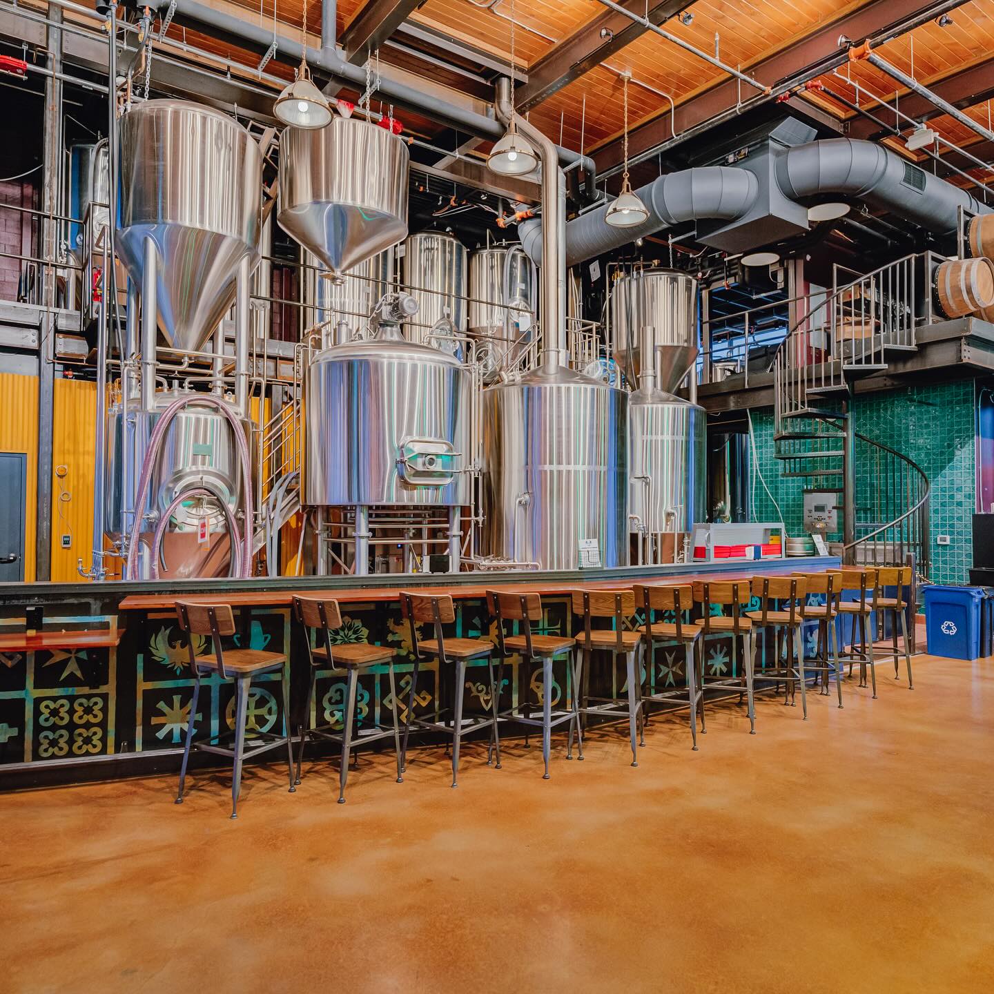 Brewery interior featuring large stainless steel tanks and a long bar.