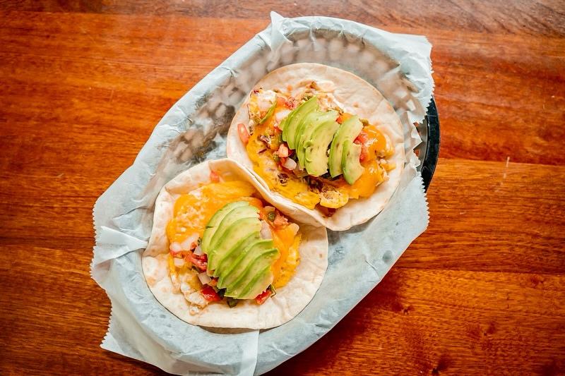 Two tacos with eggs, cheese, pico de gallo, and avocado slices.