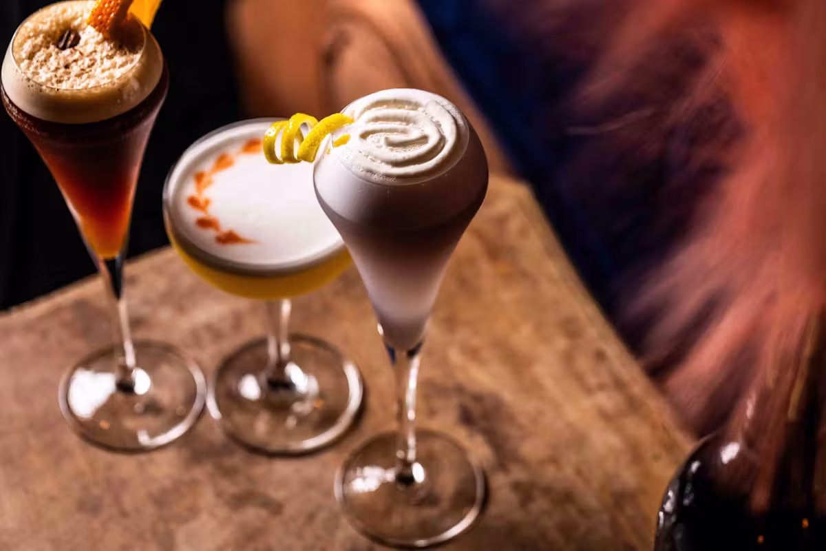 Three cocktails with foam, citrus, and coffee bean garnishes.