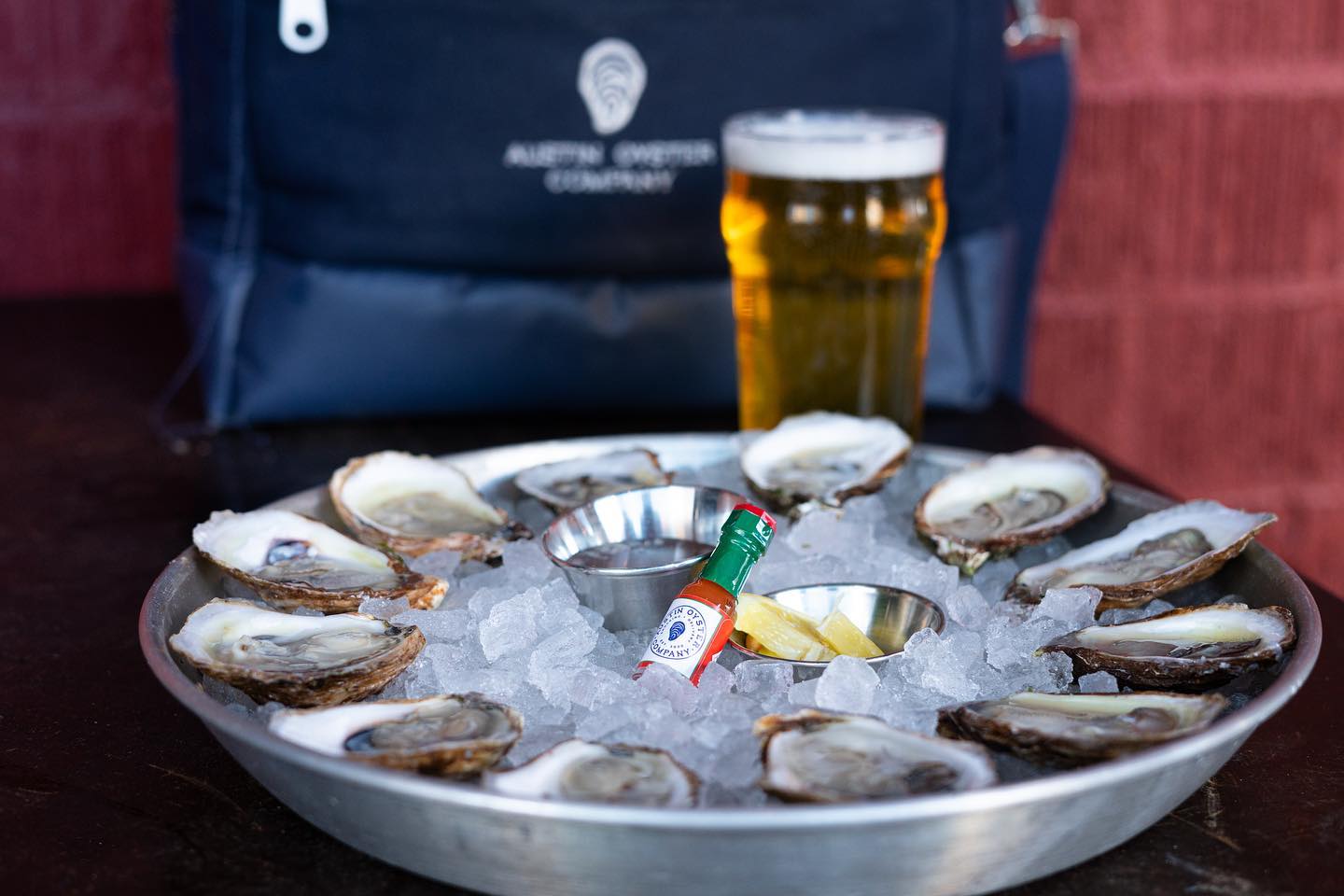 A dozen oysters on ice with hot sauce, lemon, and a beer.