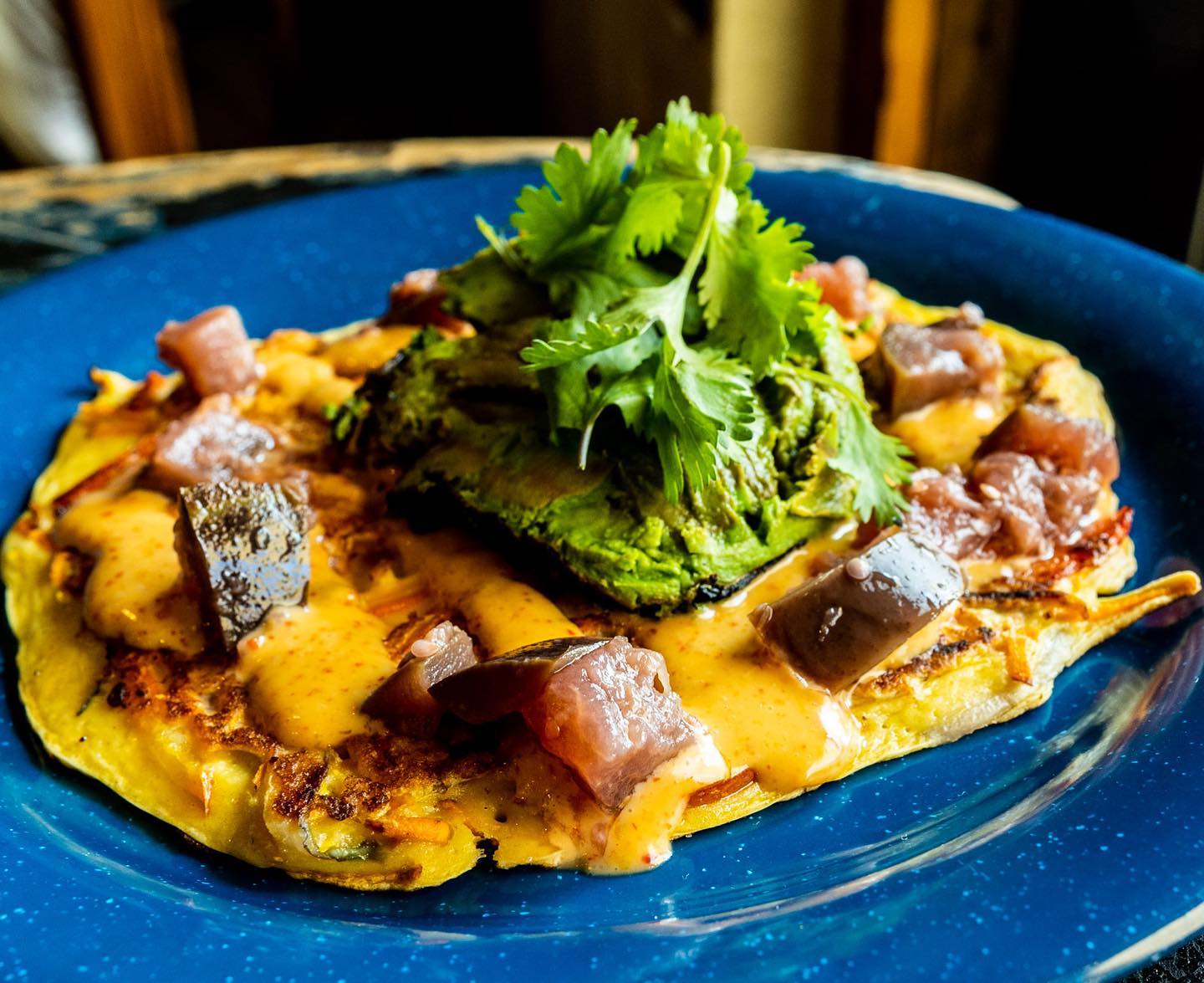 Savory pancake with cubed fish, mashed avocado, sauce, and cilantro.