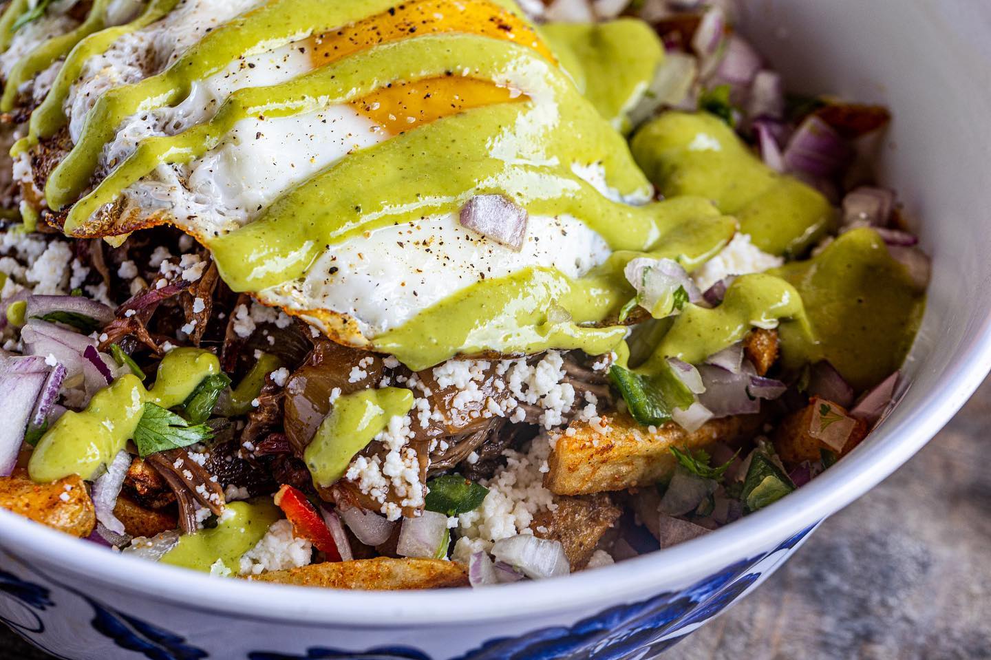 Bowl of fried eggs, shredded meat, green sauce, and cheese.