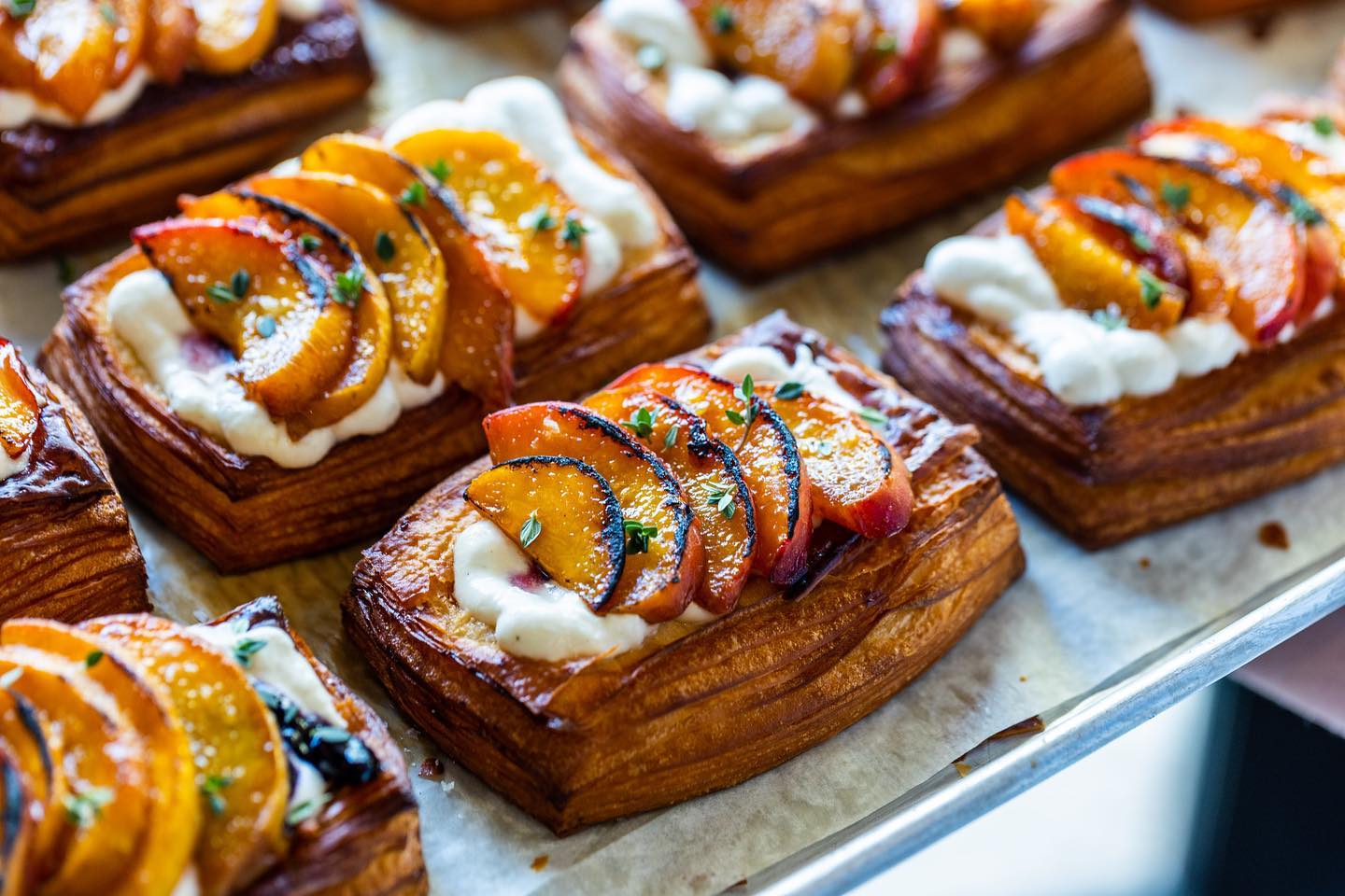 Golden pastries topped with cream, roasted peaches, and green herb sprigs.
