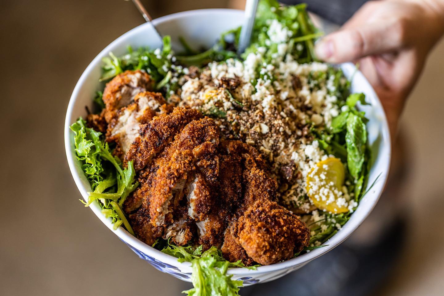 Bowl of crispy chicken, mixed greens, and various crumbled toppings.