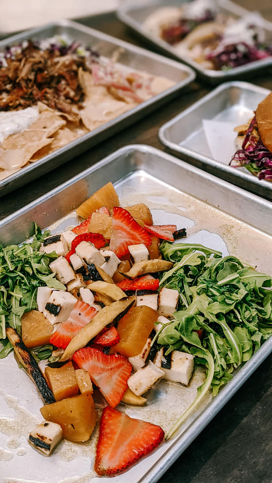 Metal trays with a meal including salad, nachos, and a burger.