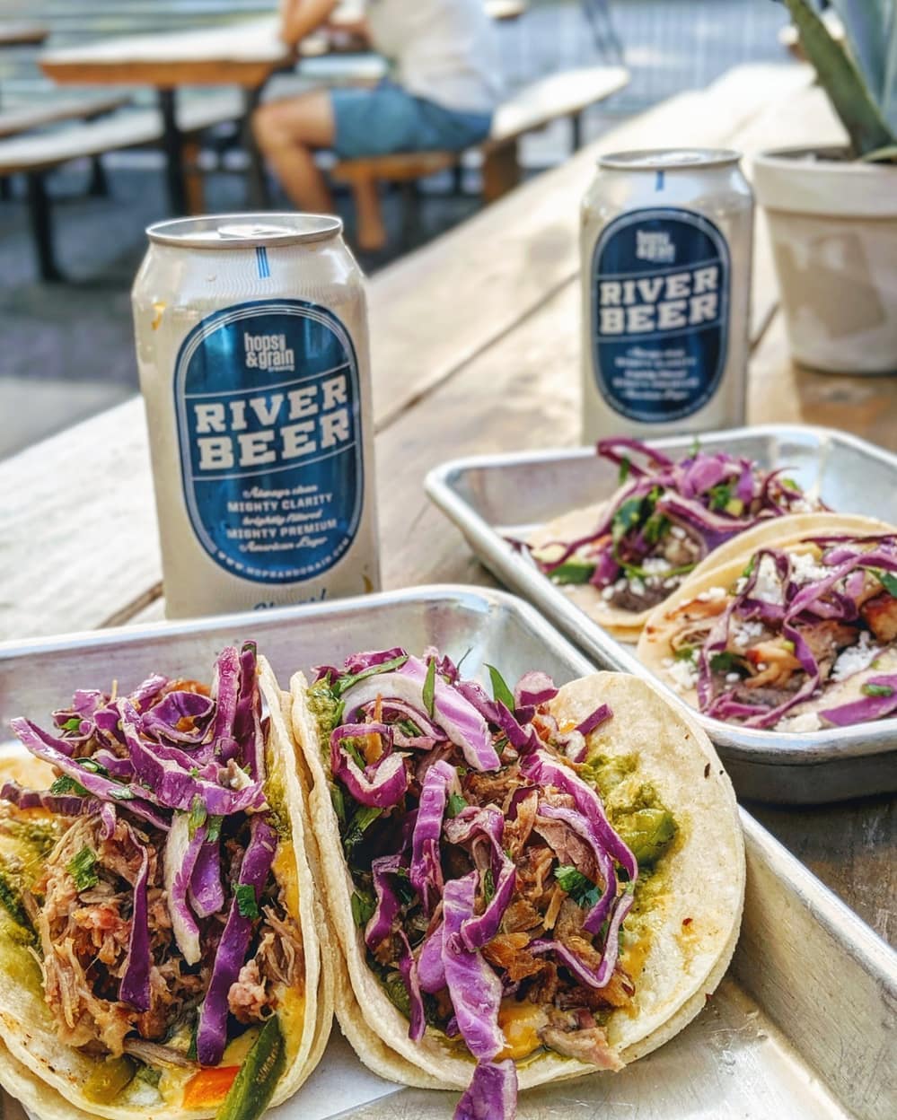 Tacos with purple cabbage and pulled pork, alongside River Beer cans.