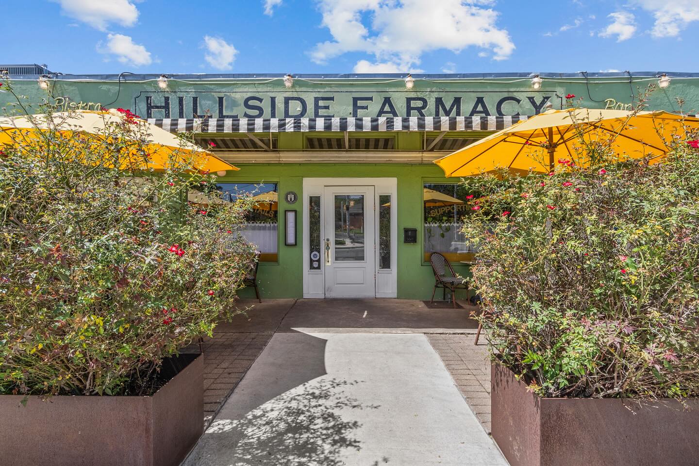 Green Hillside Farmacy building exterior with yellow umbrellas and shrubs.