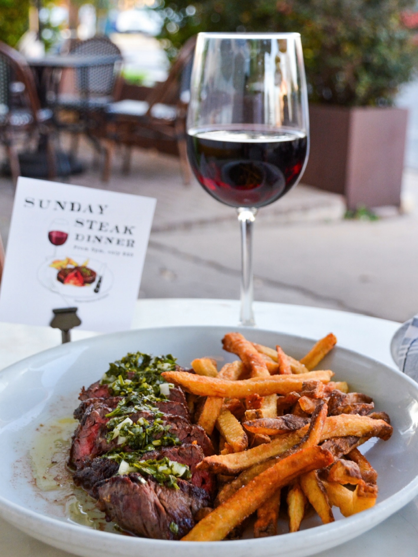 Sunday steak dinner with fries and red wine at an outdoor cafe.